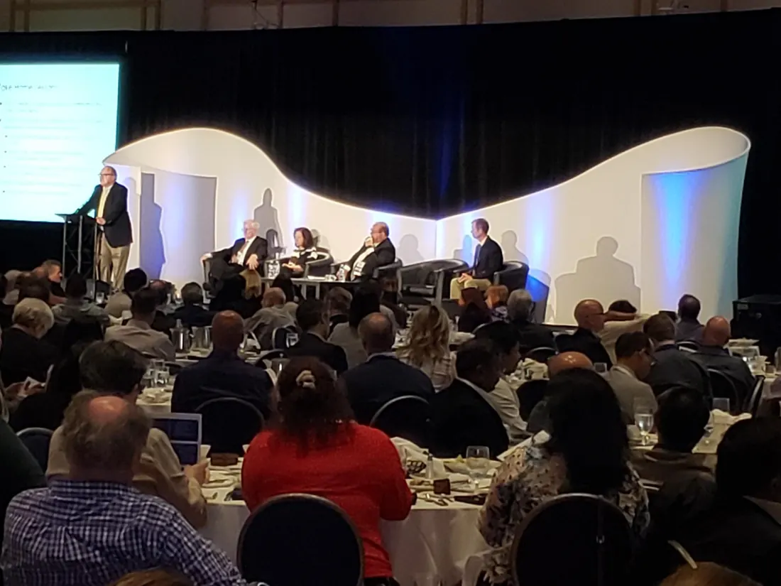 Panel session on a curved white stage with screens and lighting
